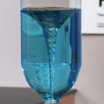 Ein Experimentglas mit blauem Wasser, das eine spiralförmige Bewegung zeigt, ideal für wissenschaftliche Dekorationen und Bildungszwecke.