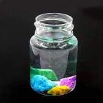 Glas mit bunten, leuchtenden Mineralien und Kristallen, ideal für wissenschaftliche Dekorationen und Experimente.
