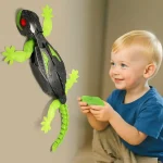 Kind spielt mit einem elektronischen Lizard-Spielzeug, das an der Wand befestigt ist, mit Fernbedienung in der Hand, im Wohnzimmer.