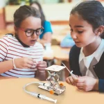 Zwei Kinder bauen ein wissenschaftliches Experiment mit einem kleinen mechanischen Gerät in einem Klassenzimmer.