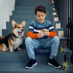 Junge sitzt auf Treppe, spielt mit einem Rubik's Cube, neben ihm sitzt ein Hund, beide entspannt und glücklich.