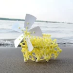 Detailliertes gelbes Molekülmodell mit weißen Rotorblättern am Strand, symbolisiert wissenschaftliche Forschung und chemische Strukturen.