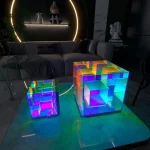 Bunte holografische 3D-Labyrinth-Modelle aus transparentem Material, beleuchtet mit LED-Lichtern, auf einem Tisch in einem modernen Wohnzimmer.