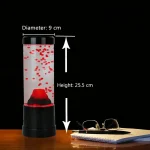 Wissenschaftlicher Blubberblase-Generator mit rotem Wasser, 25,5 cm hoch und 9 cm Durchmesser, auf einem Holzschreibtisch neben Brille und Notizbuch.