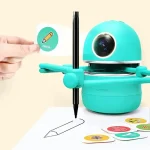 Ein blauer, humanoider Roboter zeichnet mit einem Stift auf Papier, während eine Hand eine Karte mit einem Bleistift-Symbol hält. Das Bild zeigt ein interaktives Lernspielzeug für Kinder.