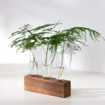 Elegante Blattdekoration mit drei Glasvasen auf einem rechteckigen Holzsockel, ideal für moderne Raumgestaltung und wissenschaftliche Dekoration.