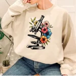 Pullover mit Mikroskopmuster, umgeben von bunten Blumen, perfekt für Wissenschafts- und originelle Dekorationsliebhaber.