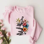 Schauen Sie sich diese Illustration eines Mikroskops, umgeben von bunten Blumen, an, perfekt für ein originelles und wissenschaftliches T-Shirt.