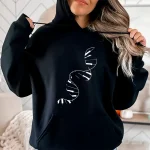 Eine Frau trägt einen schwarzen Kapuzenpullover mit einem weißen Doppelhelix-DNA-Muster, das Wissenschaft und Genetik in einem lässigen Stil illustriert.
