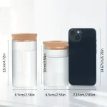 Zwei transparente Glasbehälter mit Korkdeckel neben einem schwarzen Smartphone, ideal für wissenschaftliche oder dekorative Zwecke.