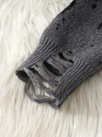 Nahaufnahme eines verzierten, grau verfärbten Strickpullovers mit Rissen und Fransen, auf weißem, flauschigem Hintergrund.