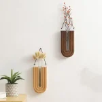 Zwei stilvolle Holzvasen in U-Form, dekoriert mit Trockenblumen, an einer weißen Wand. Perfekt für moderne Inneneinrichtung und Dekoration.
