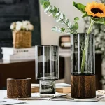 Elegante Blumenvasen aus Glas mit Holzsockel, ideal für moderne Dekorationen und Blumenarrangements. Perfekt für stilvolle Wohnräume und Tischdekorationen.